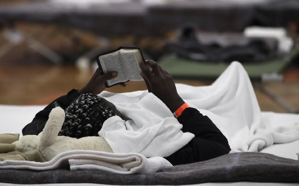 In this June 13, 2019 photo, a migrant woman reads a Bible as she rests inside the Portland Exposition Building in Portland, Maine. Maine's largest city has repurposed the basketball arena as an emergency shelter in anticipation of hundreds of asylum seekers who are headed to the state from the U.S. southern border. Most are arriving from Congo and Angola. (AP Photo/Elise Amendola)