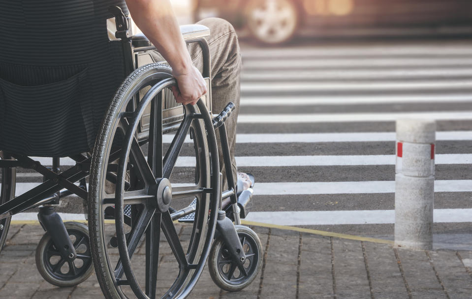 Disabled man on wheelchair preparing to cross the road on pedestrian crossing, copy space.