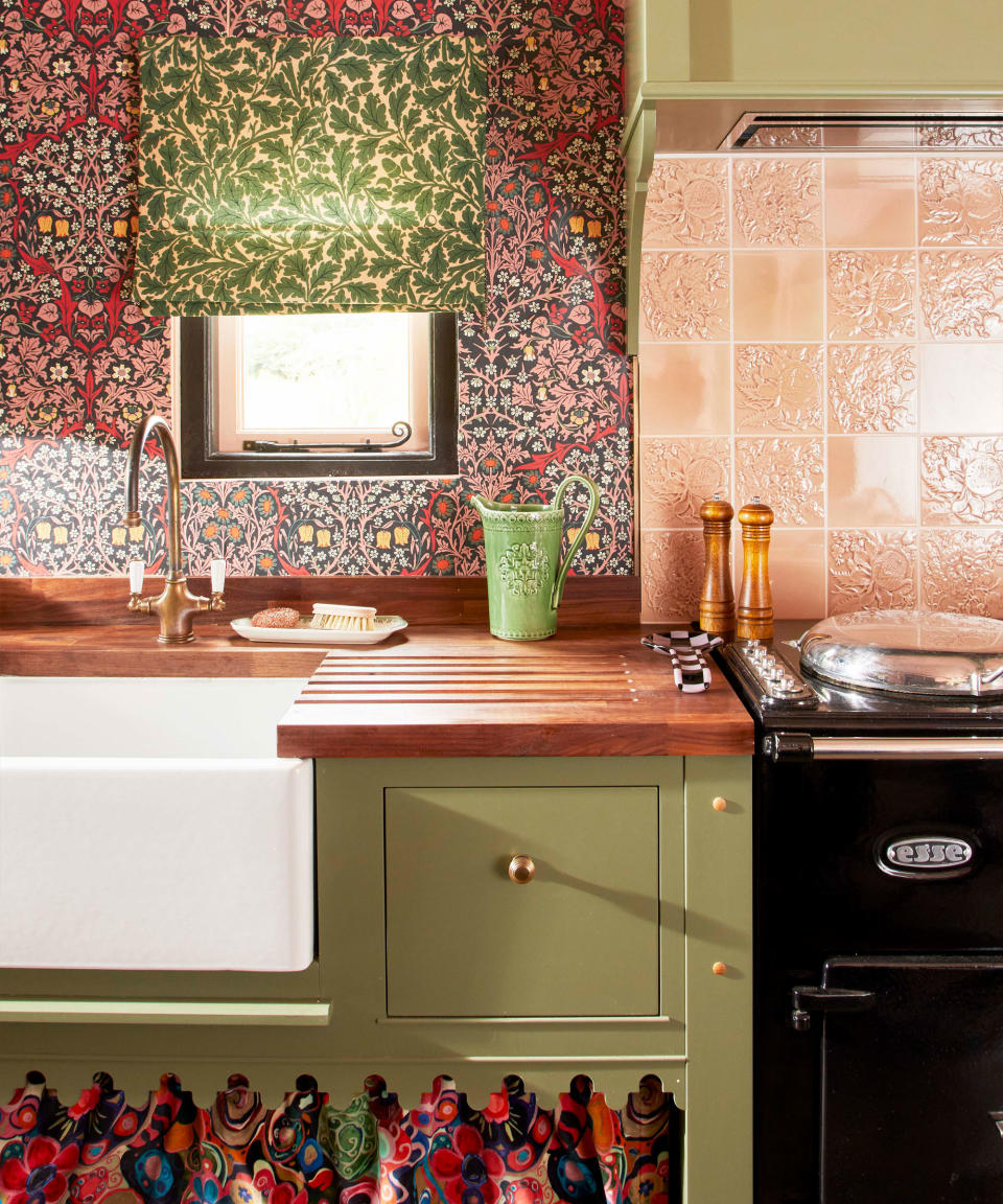 Colorful kitchen with floral patterned wallpaper, blind, green cabinetry, patterned cupboard skirt.