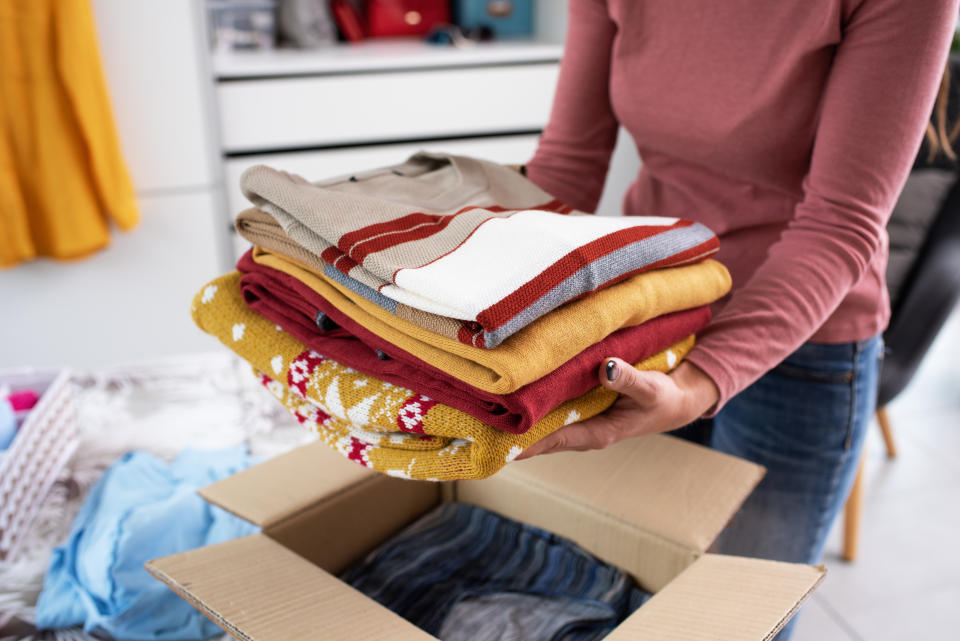 Person holding a pile of neatly folded clothes on top of an open cardboard box