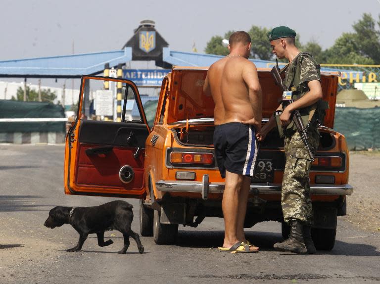 An Ukrainian border guard checks passing cars at a checkpoint in Pletnyovka on the Ukraine-Russia border, where a Russian humanitarian convoy is to cross the border on August 13, 2014