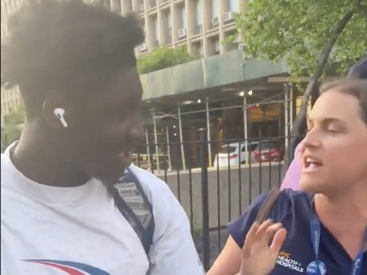 A screenshot of the viral video where a Black teen with a backpack and white T-shirt is seen arguing with a white women in hospital-worker clothes on the side of a street.