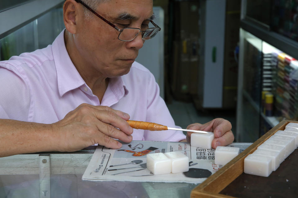 In this April 18, 2019, photo, Cheung Shun-king, 65-year-old maker of the popular table-top game mahjong tiles, engraves a character on a tile in his decades-old store 100 square feet downstairs shop in a Kowloon's old neighborhood of Hong Kong. Hand-carved mahjong tiles is a dying art in Hong Kong. But a small 50-year-old mahjong tile shop is trying to revive the heritage/raise people's interest by organizing hand-craved tile class to keep the tradition alive. (AP Photo/Kin Cheung)