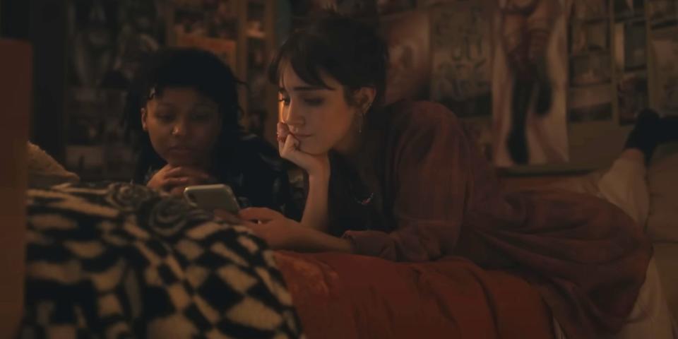Two girls lay on a bed in a still from "Dumb Money."