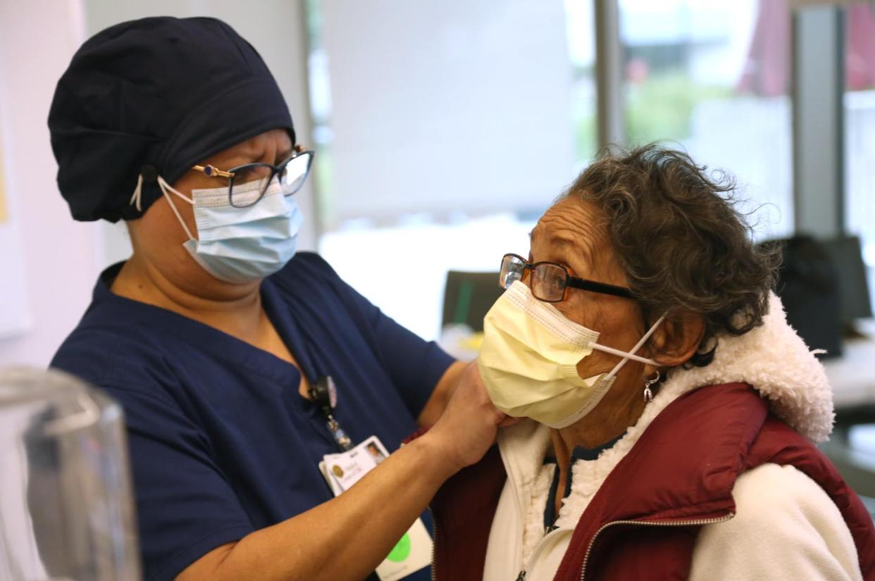 <span class="caption">Maria Saravia, a worker at the University of Southern California's Keck Hospital, adjusts her mother's mask before her COVID-19 vaccination.</span> <span class="attribution"><a class="link " href="https://www.gettyimages.com/detail/news-photo/maria-saravia-left-an-environmental-services-worker-at-keck-news-photo/1230785871" rel="nofollow noopener" target="_blank" data-ylk="slk:Genaro Molina/Los Angeles Times via Getty Images;elm:context_link;itc:0;sec:content-canvas">Genaro Molina/Los Angeles Times via Getty Images </a></span>