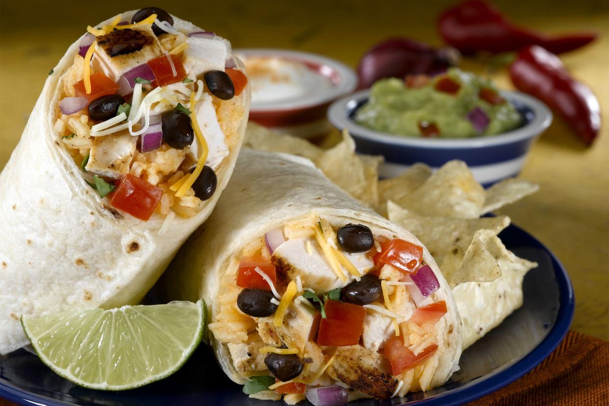 Cracking chicken burrito with tortilla chips and a slice of lime on a dark blue plate with guacamole and condiments in the background