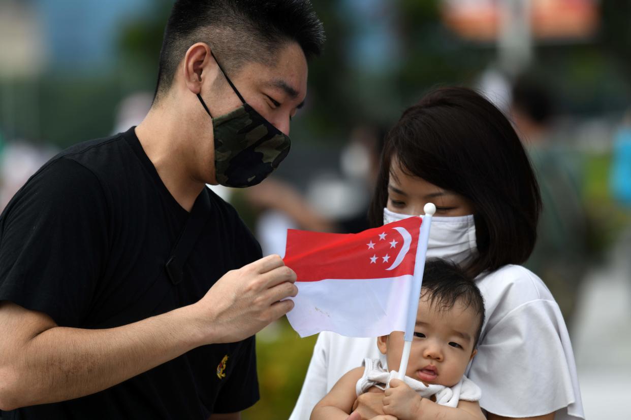 A couple attends to their child as the infant holds the Singapore national flag at the Merlion Park to mark the 55th National Day celebrations in Singapore on August 9, 2020. (Photo by Roslan RAHMAN / AFP) (Photo by ROSLAN RAHMAN/AFP via Getty Images)