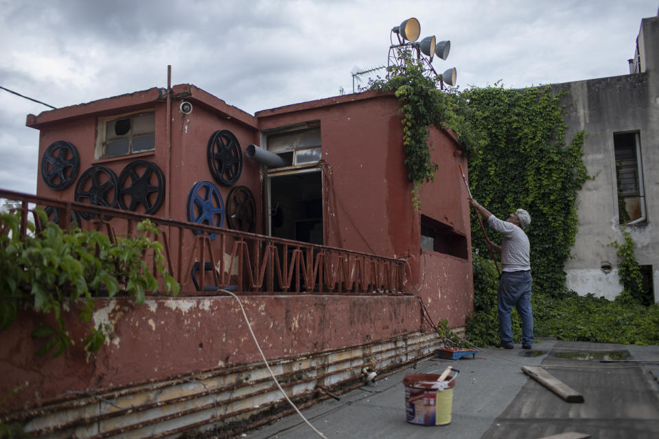 In this Friday May 29, 2020 photo projector operator Pavlos Lepeniotis paints the projection booth at the Zephyros open-air cinema that specializes in films from past decades in Athens' central Petralona district. Under the country's partial reopening after the coronavirus lockdown, open-air cinemas started operating on June 1, a month late and with considerable restrictions: Far fewer seats and no interval, both bad for revenues. (AP Photo/Petros Giannakouris)