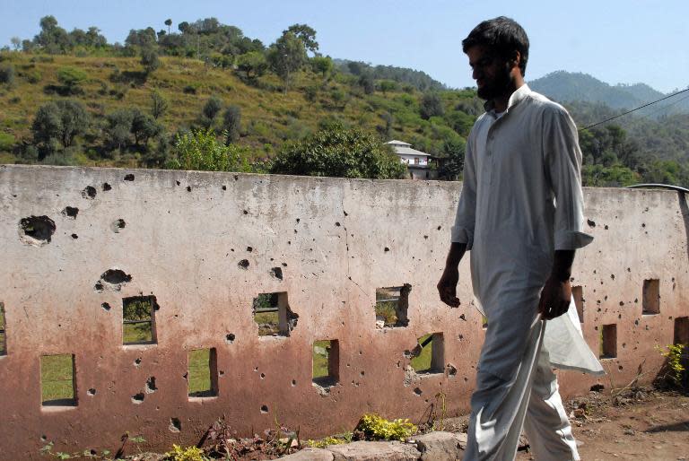 A Pakistani Kashmiri resident walks past a shrapnel-marked boundary wall hit by shelling from Indian troops at Darra Sher Khan -- near the Line of Control (LoC) which separates Indian- and Pakistani-administered Kashmir -- on October 10, 2014