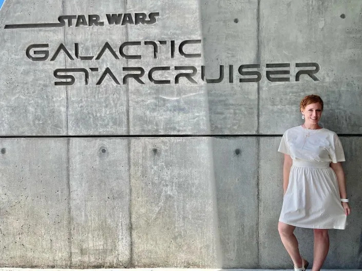 the writer in a white dress posing in front of the galactic starcruiser wall