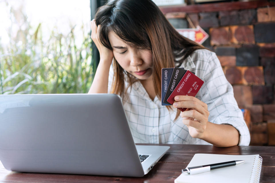 Close up of upset young Asian woman closing her eyes while holding credit cards and feeling stressed