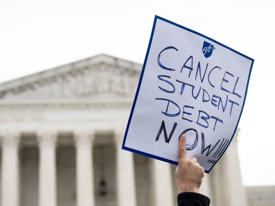 a hand holding up a sign that reads "cancel student loan debt now"