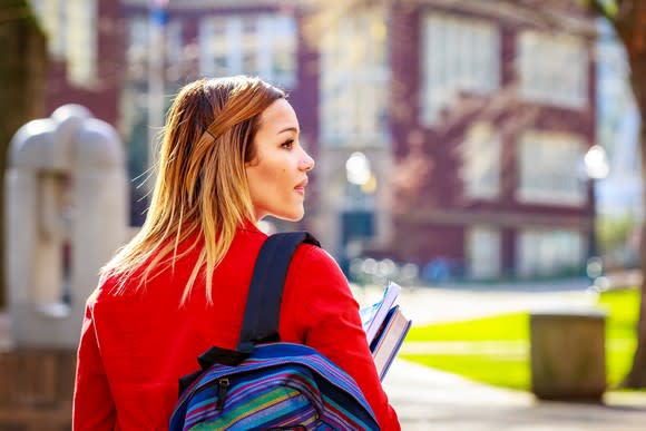 Woman wearing a backpack and holding textbooks.