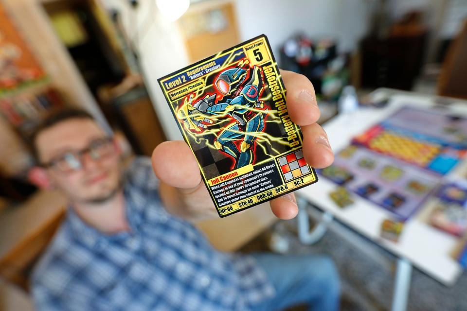 Recent UMass Dartmouth illustration graduate, Brian Fournier, holds up one of the cards for the board game he has designed.