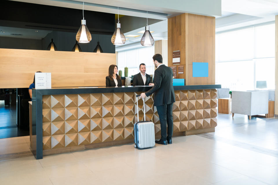 Businessman making booking at front desk with Latin receptionists in hotel lobby