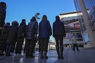 A worker walks by a group of people stand watch at an outdoor screen showing a live broadcast of the memorial service for late former Chinese President Jiang Zemin, at the Wangfujing shopping street in Beijing, Tuesday, Dec. 6, 2022. A formal memorial service was held Tuesday at the Great Hall of the People, the seat of the ceremonial legislature in the center of Beijing. (AP Photo/Andy Wong)