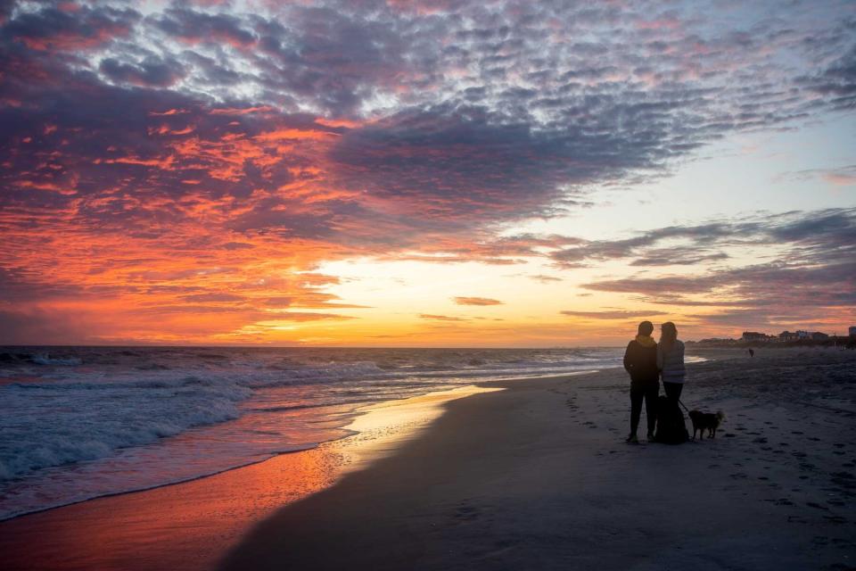 Distant landscape of Mo, the first Dog Travel Agent, and family admiring sunset over ocean at Atlantic Beach.