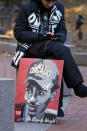 A lone demonstrator sits on a cement barrier with a Daunte Wright poster, Thursday, Dec. 2, 2021, outside the Hennepin County Government Center in Minneapolis as jury selection enters the third day for former suburban Minneapolis police officer Kim Potter. Potter, who is white, is charged with manslaughter in the April 11 shooting of Wright, a 20-year-old Black motorist, following a traffic stop in Brooklyn Center. (AP Photo/Jim Mone)