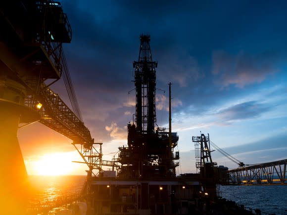An offshore oil platform with the sun rising in the background.