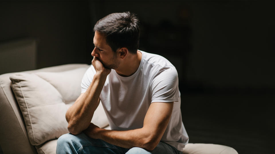 Person sitting on a couch, resting chin on hand, with a contemplative expression