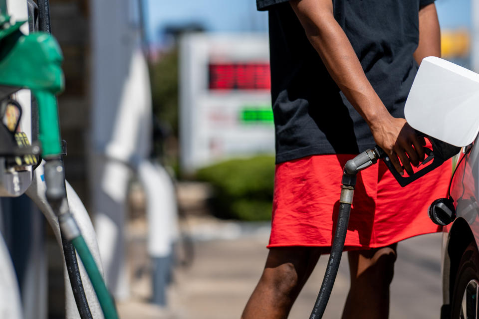 A person in red shorts pumps gas at a Shell gas station.