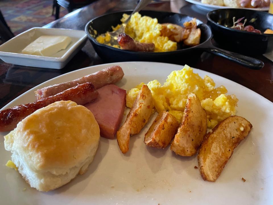 Plate of potatoes, eggs, biscuit, sausage  links, and ham.