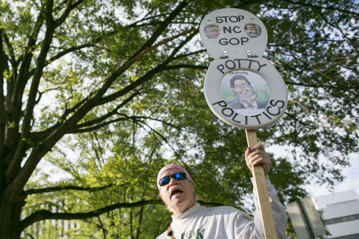 A demonstrator holds up two pieces of a toilet seat, framing a caricature of Dr. Potty, marked: Stop NC GOP, Potty Politics.