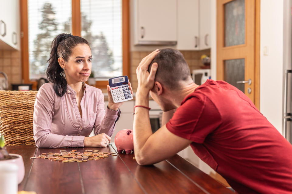 Tight family budget problems as desperate woman shows a sum on a calculator to a man with head in his hands.