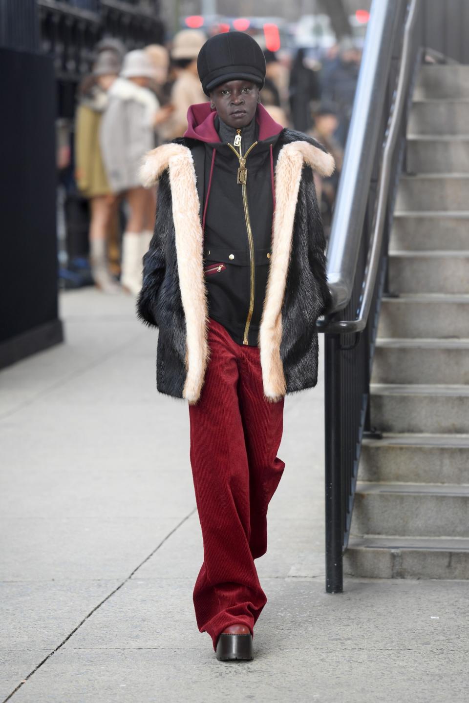 Model Alek Wek wears a loosely fitted tracksuit, black shearling-lined jacket, and black cap