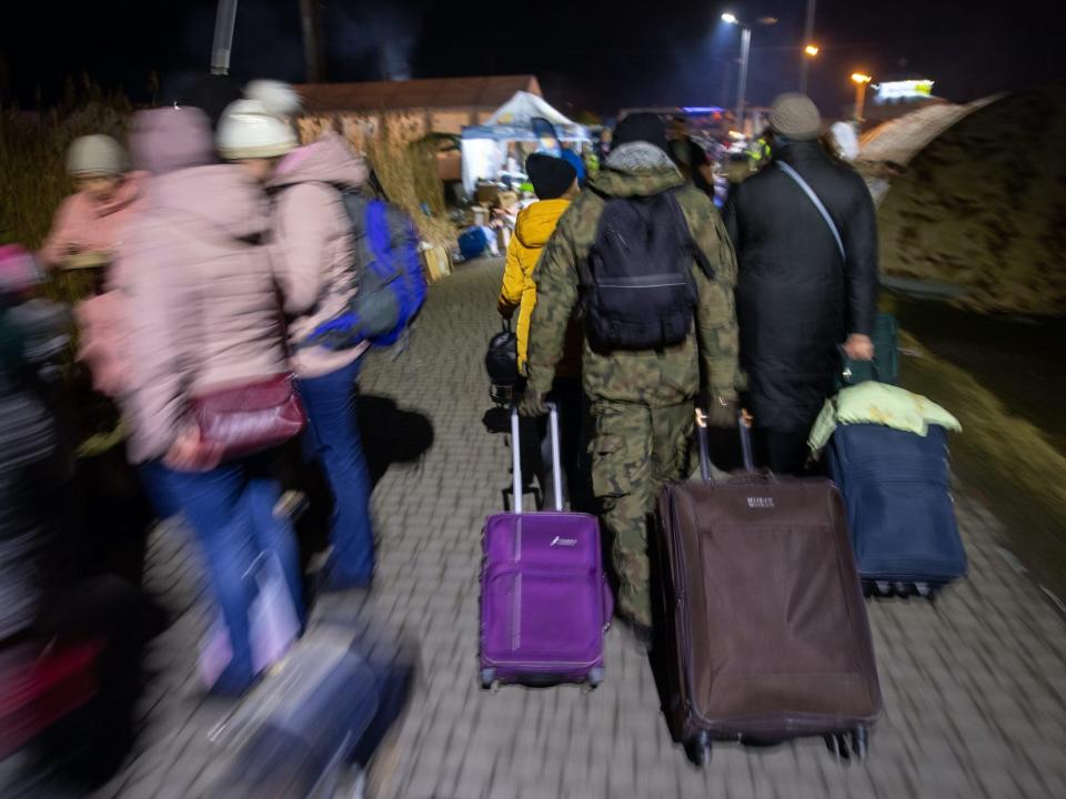 A man in camouflage clothing helps refugees from Ukraine to pull their suitcases at the border crossing in Medyka, Poland.