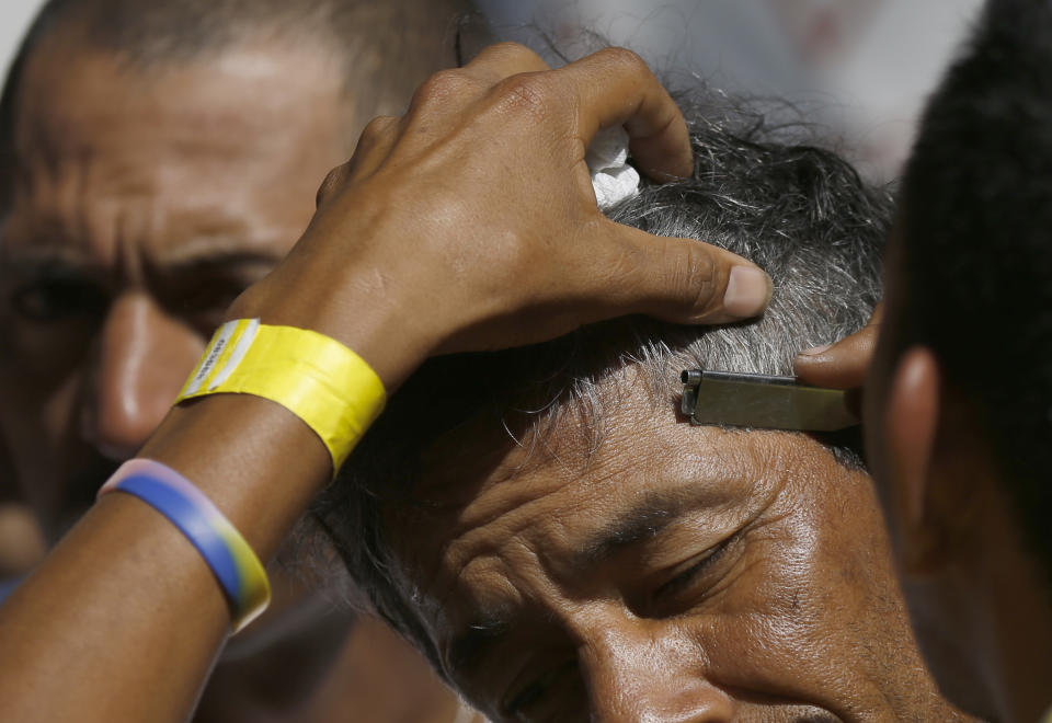 A volunteer trims the hair of a Central American migrant at the Jesus Martinez stadium in Mexico City, Tuesday, Nov. 6, 2018. Humanitarian aid converged around the stadium in Mexico City where thousands of Central American migrants winding their way toward the United States were resting Tuesday after an arduous trek that has taken them through three countries in three weeks. (AP Photo/Marco Ugarte)