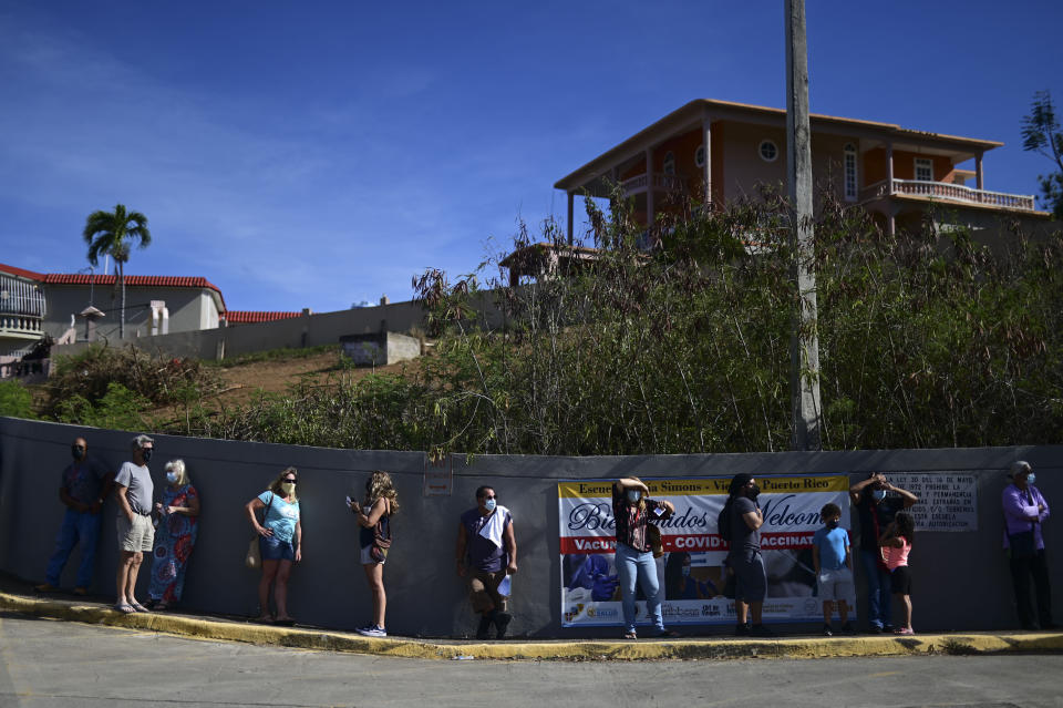 FILE - In this March 10, 2021 file photo, people stand in line outside the Maria Simmons elementary school waiting to be inoculated with the Moderna COVID-19 vaccine as part of a mass vaccination campaign, in Vieques, Puerto Rico. Puerto Rico seemed to be sprinting toward herd immunity this spring before people began letting their guard down against COVID-19 and new variants started spreading across the U.S. territory. (AP Photo/Carlos Giusti, File)