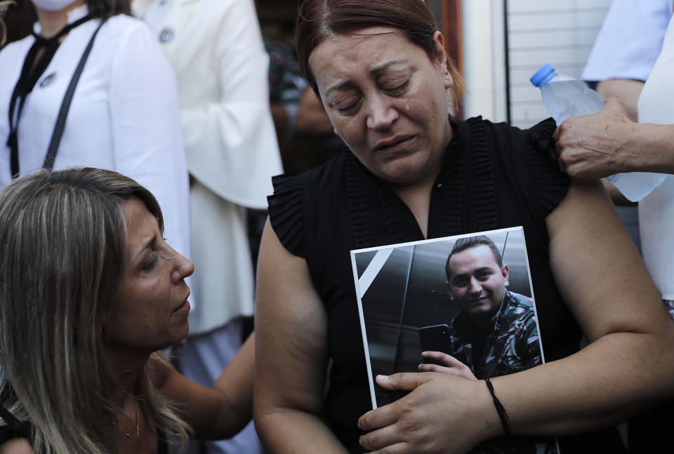 The mother of Charbel Hetti, right, one of the ten firefighters who were killed during the Aug. 4 explosion that hit the seaport of Beirut, holds his son's portrait as she mourns during his funeral at the firefighter headquarters, in Beirut, Lebanon, Monday, Aug. 17, 2020. (AP Photo/Hussein Malla)