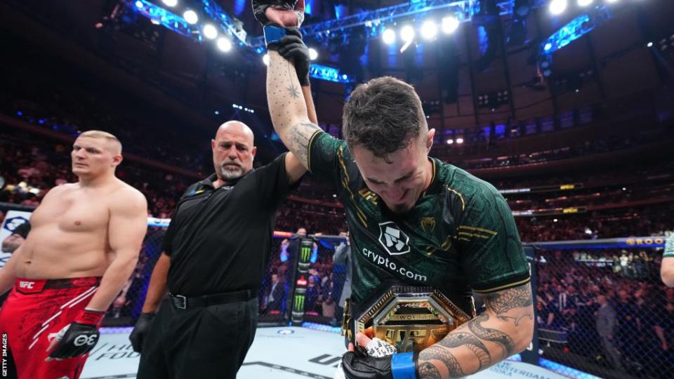 An emotional Tom Aspinall has his hand raised and a UFC belt around his waist