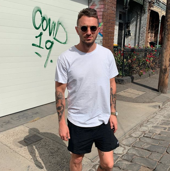 Tommy Little in a white T-shirt standing at a garage