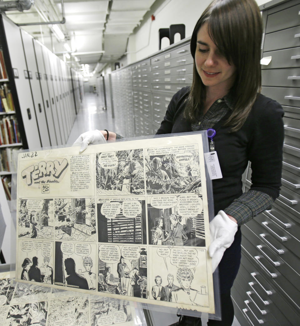 In this Wednesday, Oct. 23, 2013 photo, Caitlin McGurk holds up a cartoon titled "Terry and the Pirates" by Milton Caniff at the Billy Ireland Cartoon Library & Museum in Columbus, Ohio. The whole thing started with Caniff, the influential comic artist whose beloved “Terry and the Pirates” and “Steve Canyon” adventure strips lived in the nation’s funny papers for a half century. Caniff graduated from Ohio State University and loved the place so much he wanted his original art and other papers to be kept here forever. (AP Photo/Tony Dejak)
