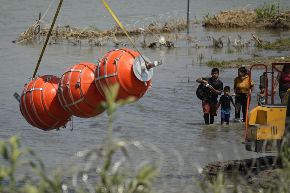 Migrantes observan unas boyas grandes que serán utilizadas como valla fronteriza en el río Bravo, a la altura de Eagle Pass, Texas, el miércoles 12 de julio de 2023. (AP Foto/Eric Gay)