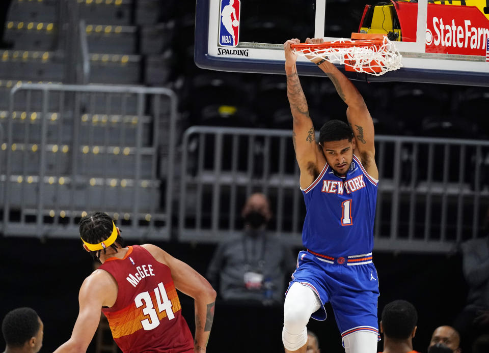 New York Knicks forward Obi Toppin, right, hangs from the rim after dunking the ball for a basket while Denver Nuggets center JaVale McGee defends in the first half of an NBA basketball game Wednesday, May 5, 2021, in Denver. (AP Photo/David Zalubowski)