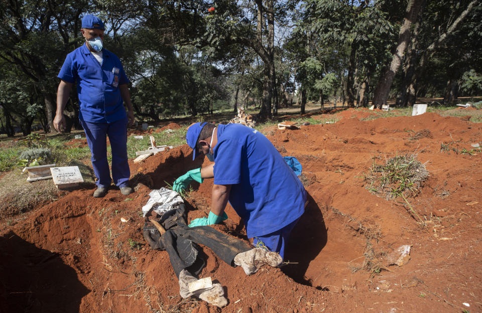 Dos trabajadores desentierran el cuerpo de una persona sepultada hace tres años en el cementerio de Vila Formosa, que no cobra a las familias por las tumbas, en Sao Paulo, Brasil, el 12 de junio de 2020. Los cuerpos sepultados hace al menos tres años, se exhuman y almacenan en bolsas de plástico para dejar sitio a más féretros, una necesidad más acuciante en la pandemia del coronavirus. (AP Foto/Andre Penner)