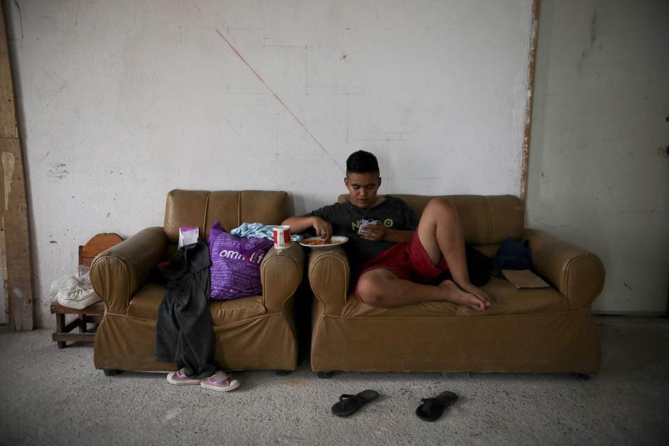 A migrant from Honduras eats a snack while looking at a smart phone inside Viento Recio church, which is serving as a migrant shelter, in Matamoros, Mexico, Thursday, Aug. 1, 2019, on the border with Brownsville, Texas. Some migrants are waiting for their names to be called from a list more than 1,000 names long to apply for asylum in the U.S. while others have recently been returned and are awaiting court dates. (AP Photo/Emilio Espejel)