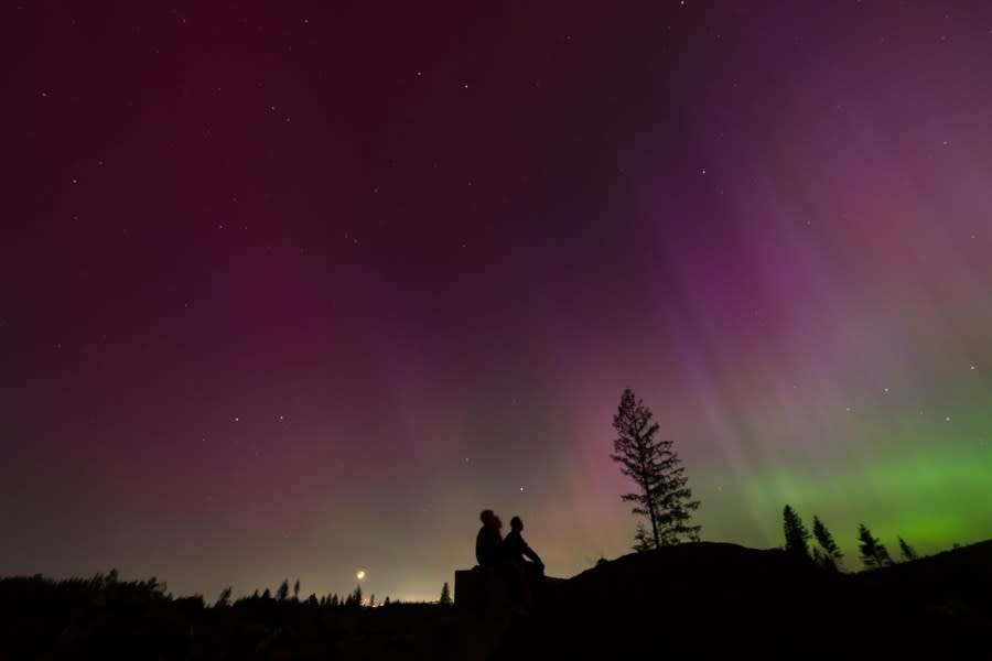 In this image taken with a long exposure, people look at the night sky towards the northern lights, or Aurora Borealis, on Friday, May 10, 2024, in Estacada, Ore. Brilliant purple, green, yellow and pink hues of the Northern Lights were reported worldwide, with sightings in Germany, Switzerland, London, and the United States and Canada. (AP Photo/Jenny Kane)