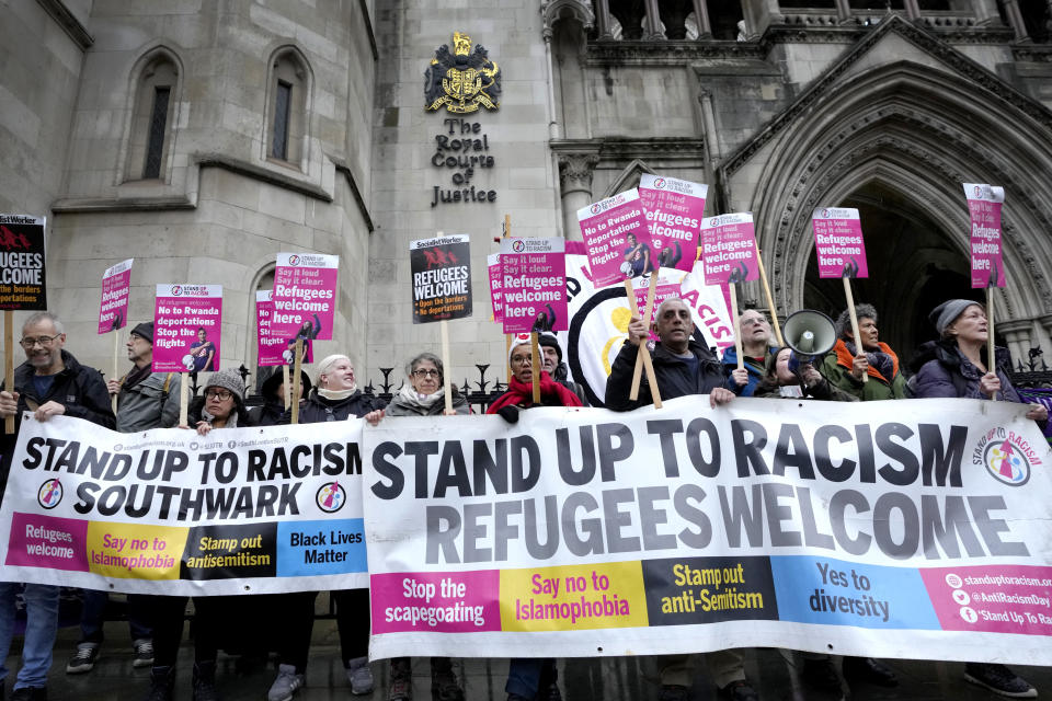 Stand Up To Racism campaigners hold banners outside the High Court in London, Monday, Dec. 19, 2022. Judges at Britain’s High Court say the U.K. government’s controversial plan to send asylum-seekers on a one-way trip to Rwanda is legal. But two judges also ruled that the government failed to consider the circumstances of the individuals it tried to deport. (AP Photo/Kirsty Wigglesworth)