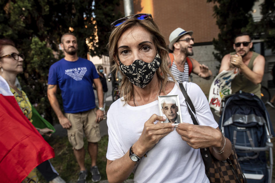 A relative of one of the victims holds his picture as a group of angry citizens protest during a ceremony to honor coronavirus victims with a Requiem concert performed in front of the cemetery in Bergamo, Northern Italy, one of the hardest-hit provinces in the onetime epicenter of the European outbreak, Sunday, June 28, 2020. (Claudio Furlan/LaPresse via AP)