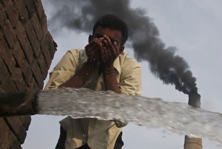 A labourer drinks water as smoke rises from a chimney of a brick factory at Togga village on the outskirts of the northern Indian city of Chandigarh in this December 6, 2009 file photo. REUTERS/Ajay Verma/Files