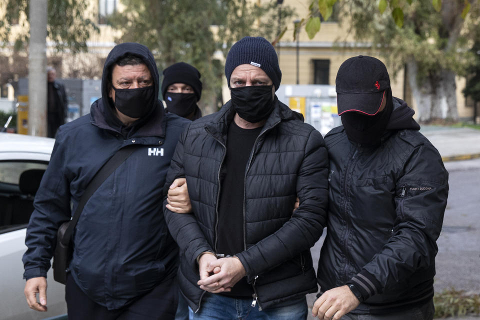 Plain-clothed policemen escort handcuffed well-known actor and director Dimitris Lignadis, center, to a magistrate's office in Athens, Sunday, Feb. 21, 2021. Lignadis, 56, the former artistic director of Greece's National Theatre, has been arrested on rape charges, police say. (AP Photo/Yorgos Karahalis)