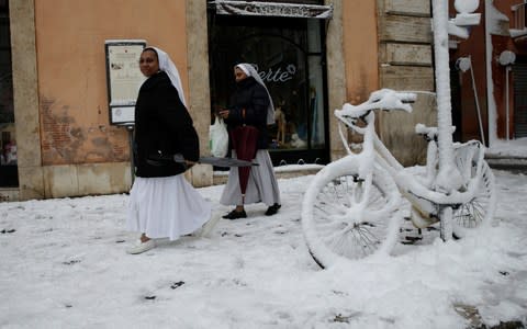 Nuns walk past a bike covered in snow in Rome, Italy - Credit: REUTERS/Max Rossi