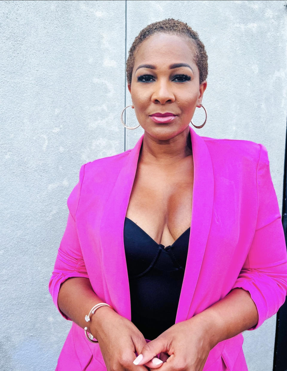 An African American woman with short hair wearing hoop earrings, in a fuchsia jacket and black top.