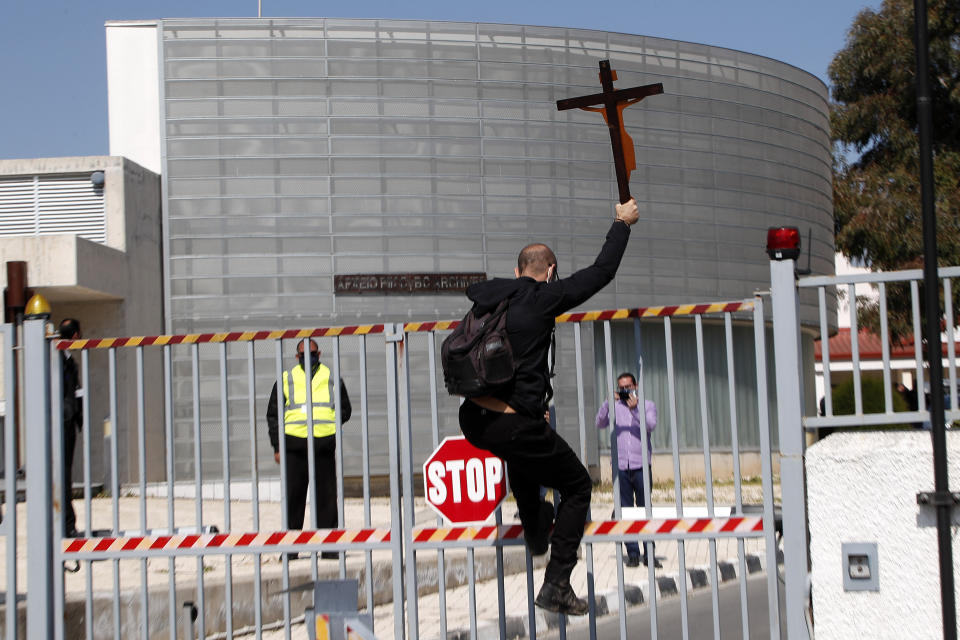 A protestor holding a cross climbs a gate outside Cyprus' national broadcasting building, during a protest, in capital Nicosia, Cyprus, Saturday, March 6, 2021. The Orthodox Church of Cyprus is calling for the withdrawal of the country’s controversial entry into this year’s Eurovision song context titled “El Diablo”, charging that the song makes an international mockery of country’s moral foundations by advocating “our surrender to the devil and promoting his worship.” (AP Photo/Petros Karadjias)