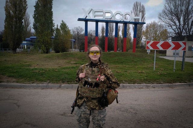 A Ukrainian female soldier poses for a photo against a Kherson sign in the background