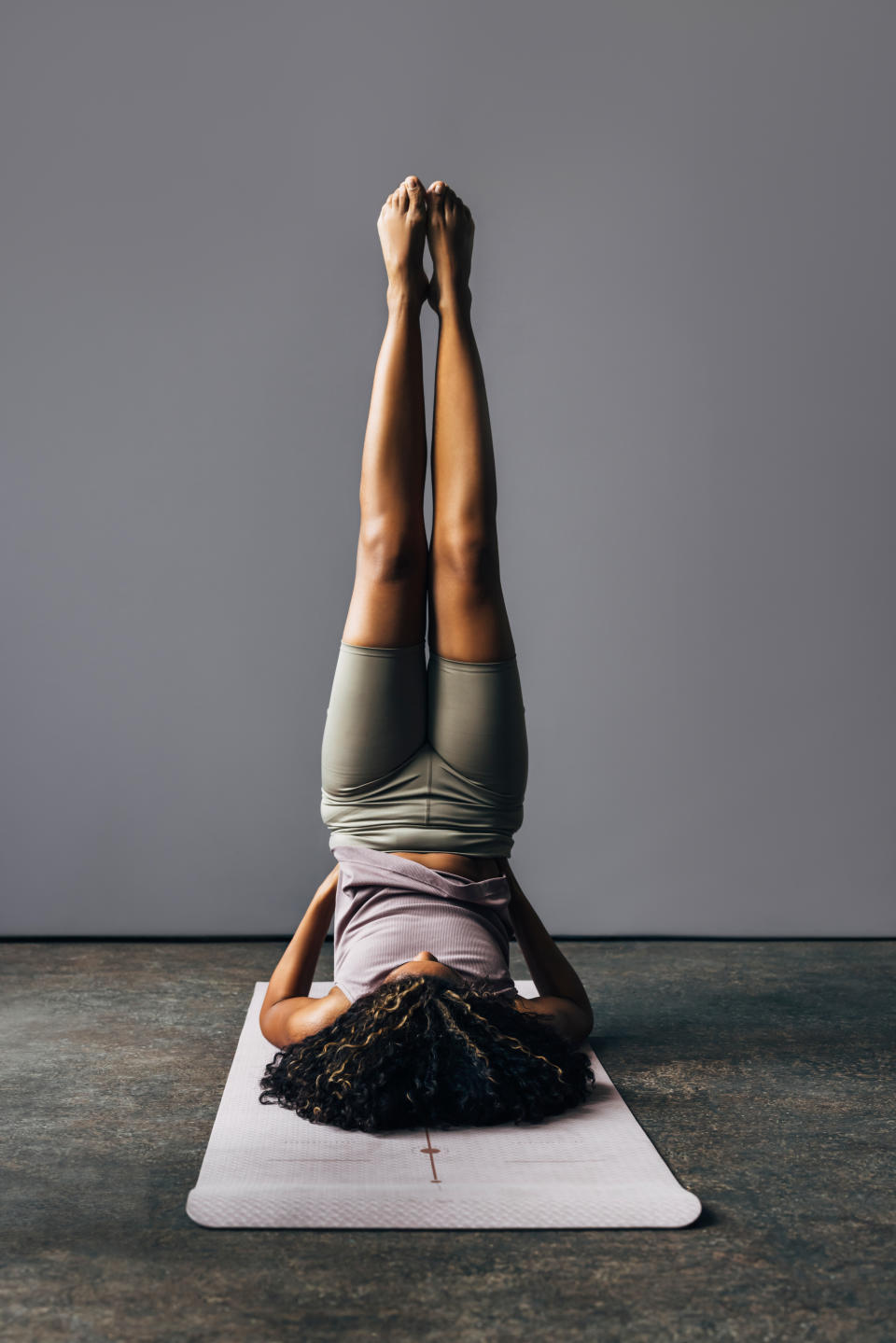 A Latin female athlete doing a handstand while being on yoga mat